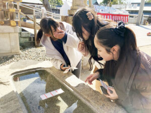 水に浮かべると文字が出てくるおみくじ「水みくじ」に注目する派遣生たち。